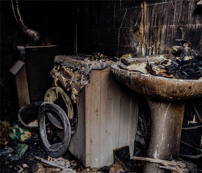 a fire damaged bathroom with soot covering everything and debris everywhere