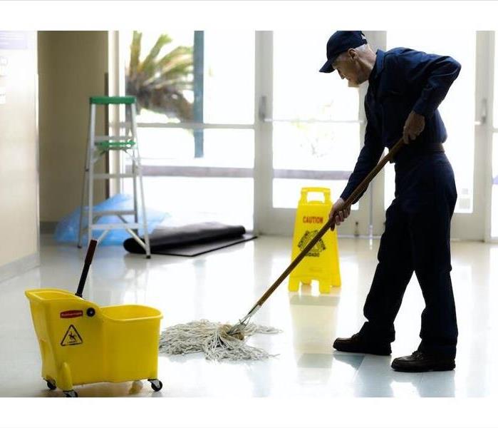 Male mopping a white floor with a yellow bucket and sign