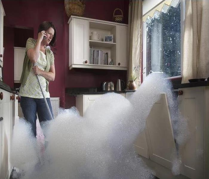 suds emitting from dishwasher and woman on phone